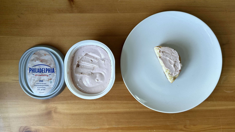 Strawberry cream cheese is shown on a bagel and in the container.