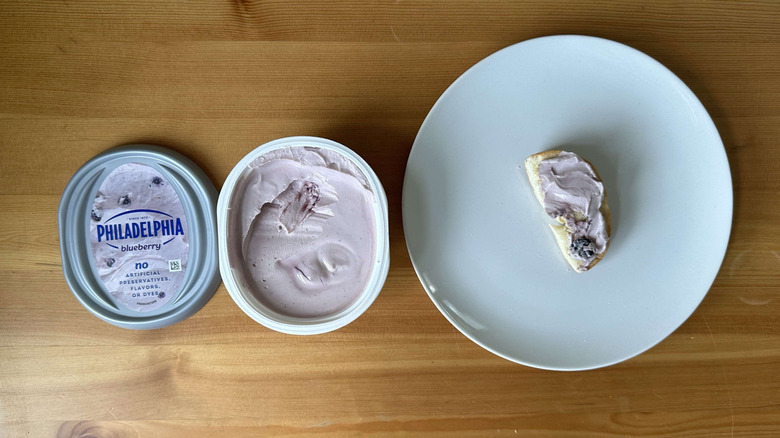 Blueberry cream cheese is shown on a bagel and in the container.