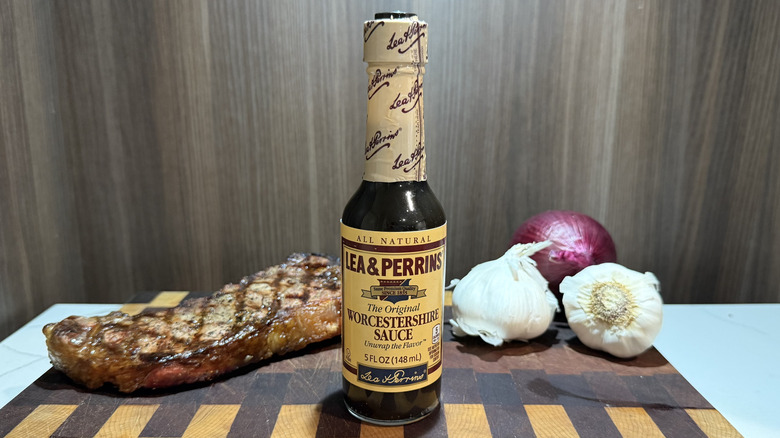 a bottle of Lea & Perrins Worcestershire sauce with a grilled steak, garlic bulbs, and red onion
