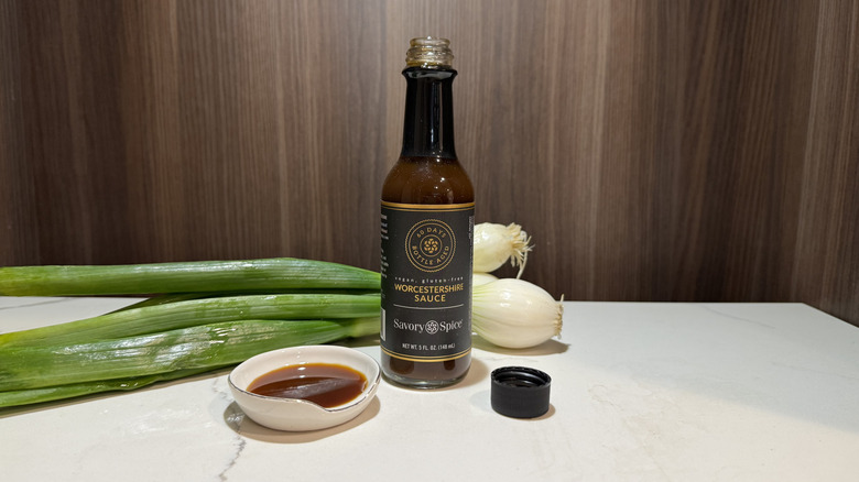 a bottle of Worcestershire sauce, some green onion bulbs, and a dish of sauce