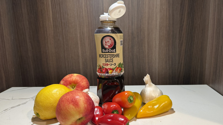 A bottle of bull-dog Worcestershire sauce surrounded by apples, peppers, garlic and lemon