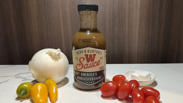 A bottle of Bear & Burton's W Sauce with an onion, yellow peppers, sugar cubes, and cherry tomatoes