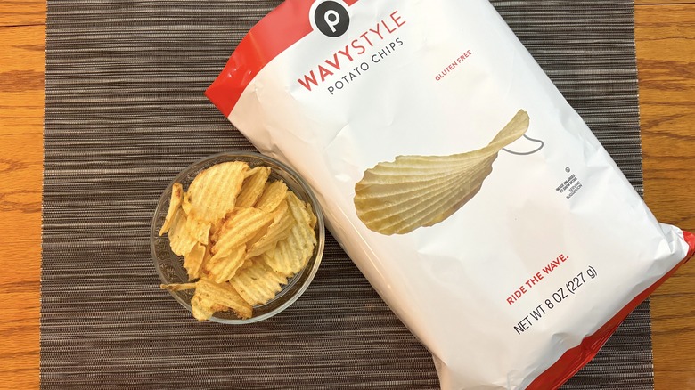 Publix wavy style potato chips in bag and glass bowl on black placemat on wooden table in bag and glass bowl on black placemat on wooden table