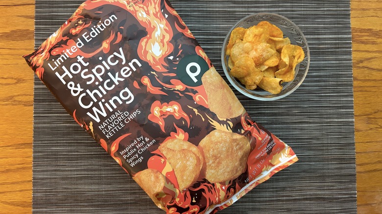 Publix hot & spicy chicken wing kettle chips in bag and glass bowl on black placemat on wooden table in bag and glass bowl on black placemat on wooden table