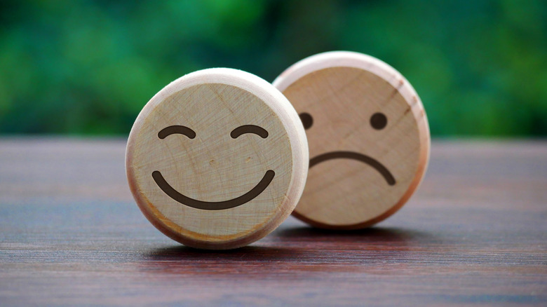 Two round wooden shapes one with a smiling face and one with a sad face on a wooden table in front of a green background