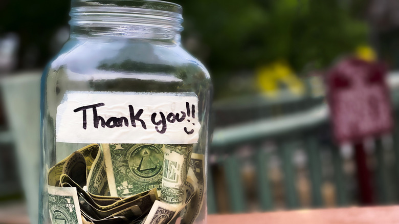 glass tip jar half filled with dollar notes and a sign on the jar that says Thank You