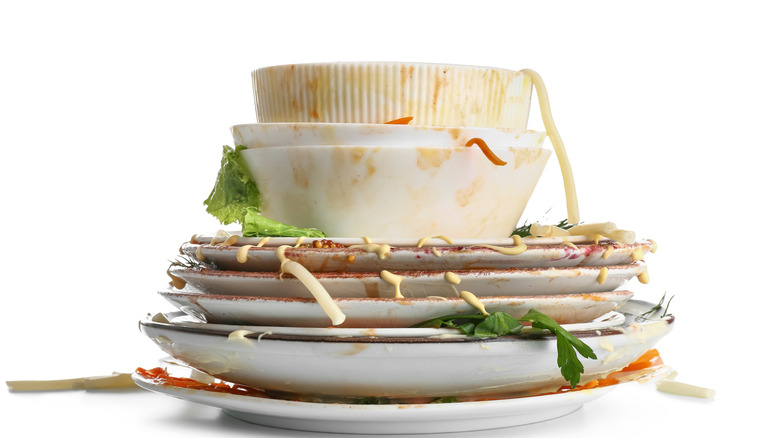Stack of dirty white dishes covered in food against a white background