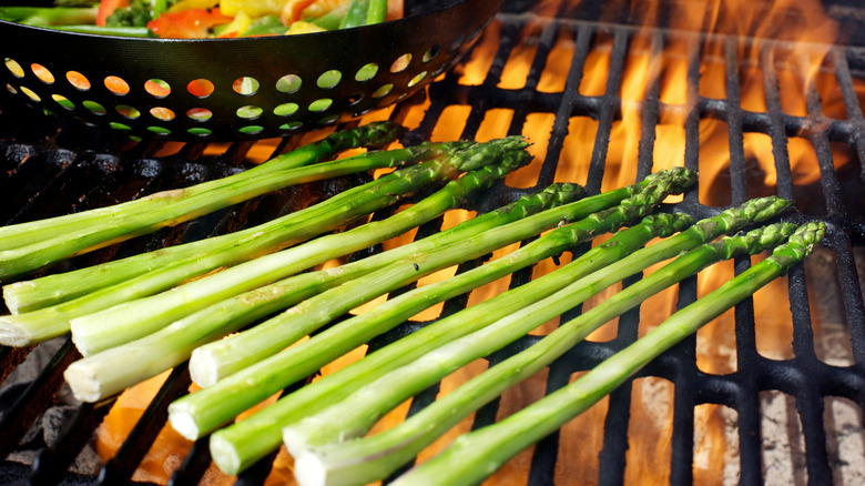 Asparagus being grilled next to a pan of vegetables