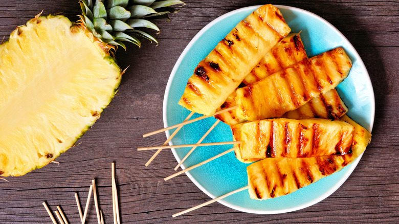 Slices of grilled pineapple served on skewers on a plate