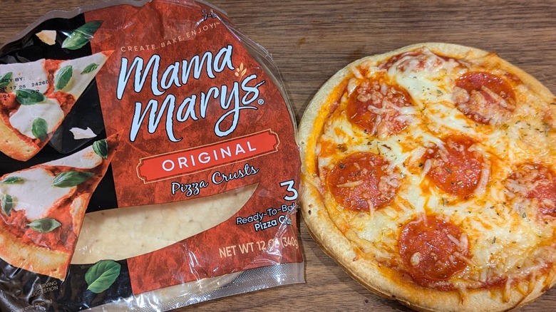 Small bag of Mama Mary's original pizza crusts next to small pepperoni pizza on wood board