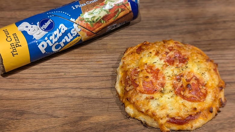 Pillsbury pizza dough tube next to mini pepperoni pizza on wood board