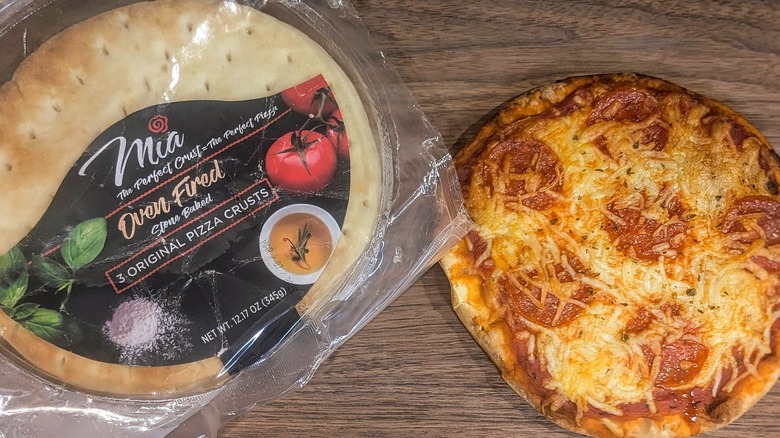 Bag of small pizza crusts next to small, cheesy, pepperoni pie on wood board