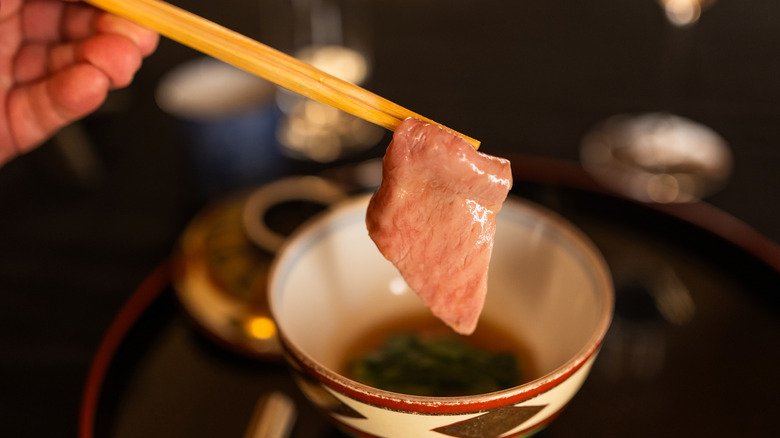 dipping a piece of beef into a soy sauce