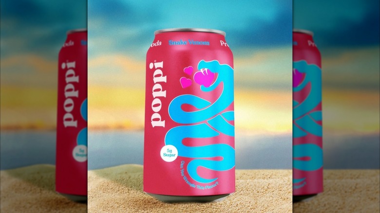 can of poppi soda sitting on sand with the ocean background