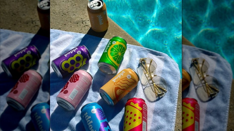 multple flavors of poppi soda laid out on a towel by the pool