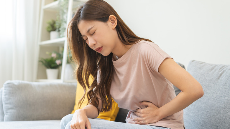 woman leaning over and holding stomach, squinting in pain