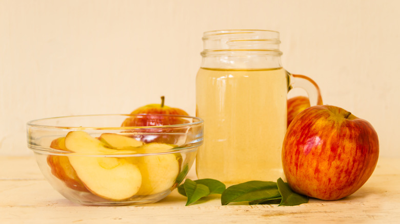 jar of apple cider vinegar with apples cut up in a bowl and whole apples to the side