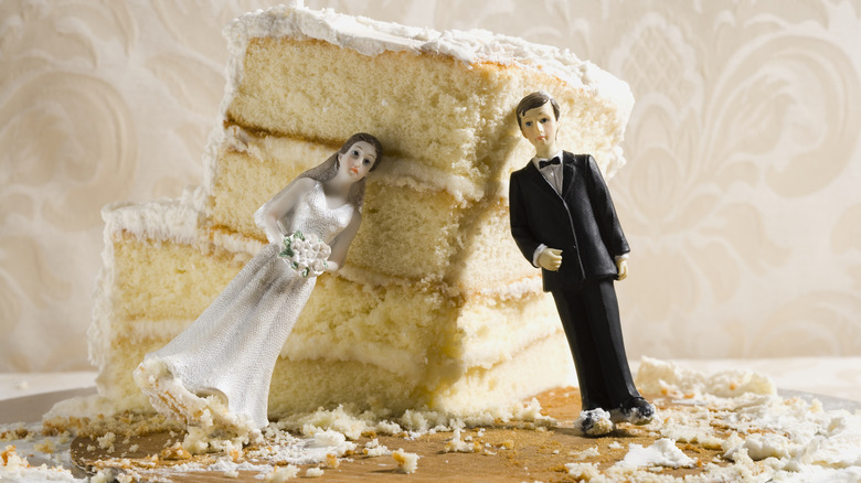 A slice of a wedding cake with bride and groom cake toppers leaning against it