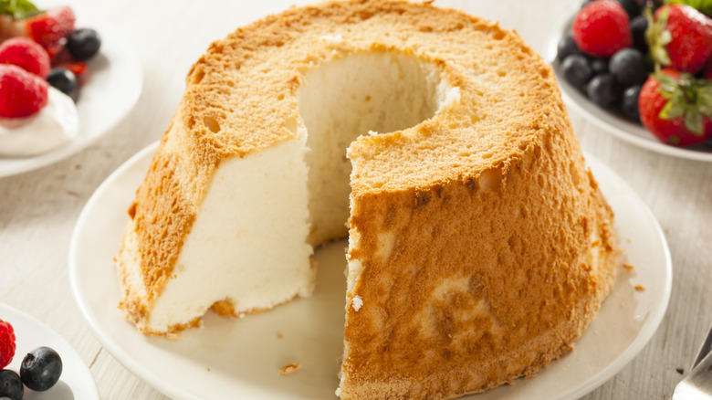 Angel food cake with slice missing on plate and fresh berries on separate plates