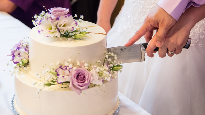 Two hands holding knife and cutting into a wedding cake with sugar flowers