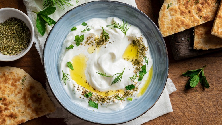 Labneh in bowl with olive oil and herbs, surrounded by bread