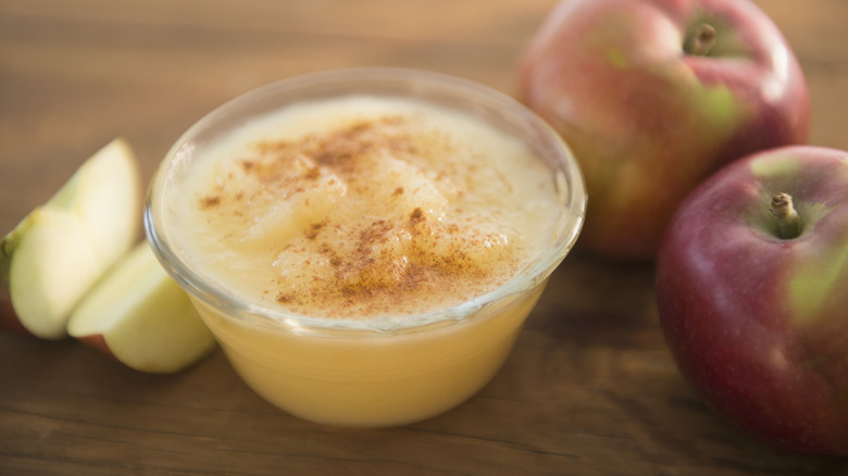 Homemade apple sauce in small glass ramekin surrounded by apples