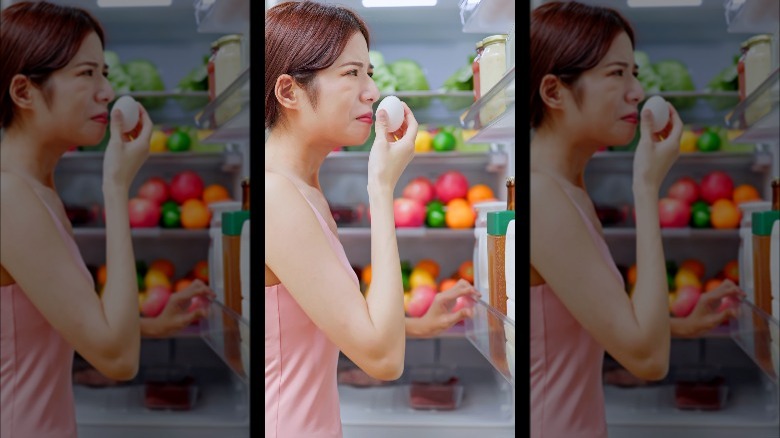 Woman smelling egg by refrigerator