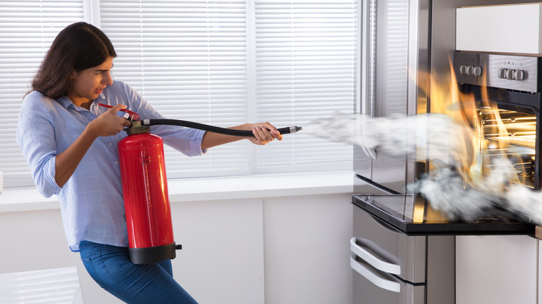 woman using fire extinguisher in kitchen