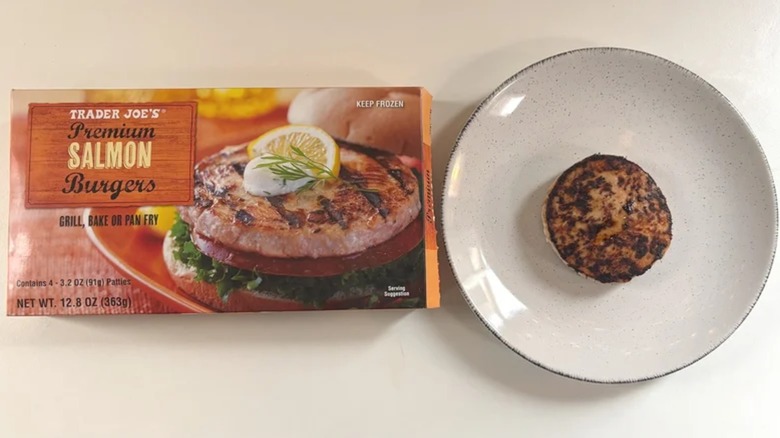 Box of Trader Joe's salmon burgers next to cooked salmon burger on white plate