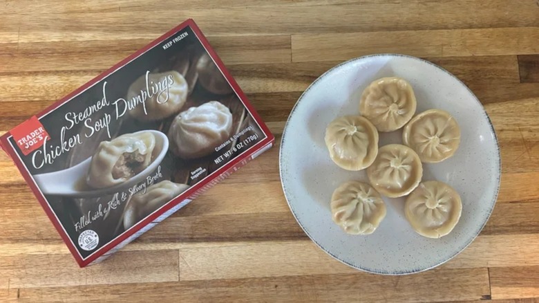 Box of Trader Joe's Steamed Chicken Soup Dumplings next to white plate of dumplings on wooden cutting board
