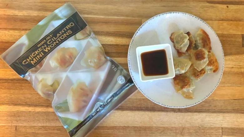 Bag of Trader Joe's Chicken Cilantro Mini Wontons next to plate of wontons and soy sauce on wooden table