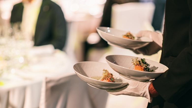 Waiter in black tie and white gloves serving food