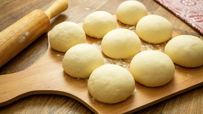 Fresh homemade pizza dough in balls on wooden cutting board