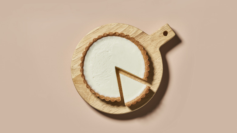 Cheesecake on wooden cutting board with one slice cut