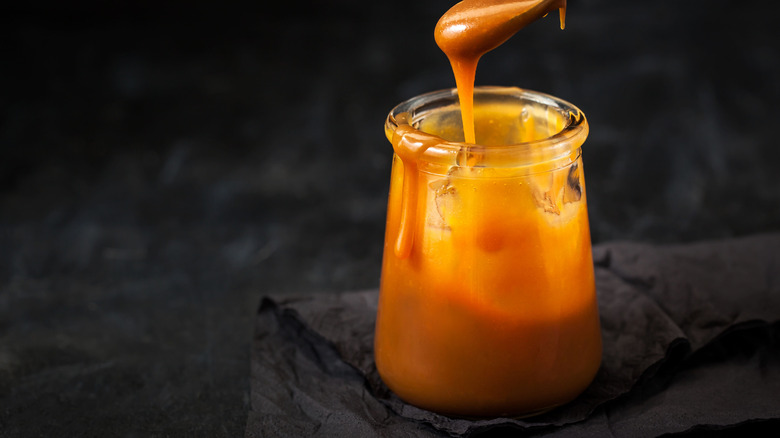 A spoon drips caramel into a jar of salted caramel.