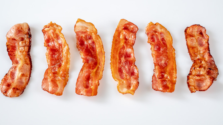 Cooked bacon strips are lined up on a white background.