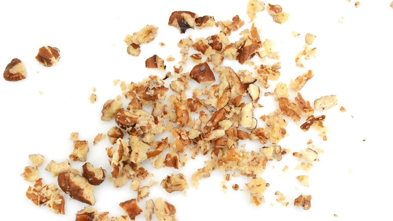 Roughly chopped pecans are spread on a white background.