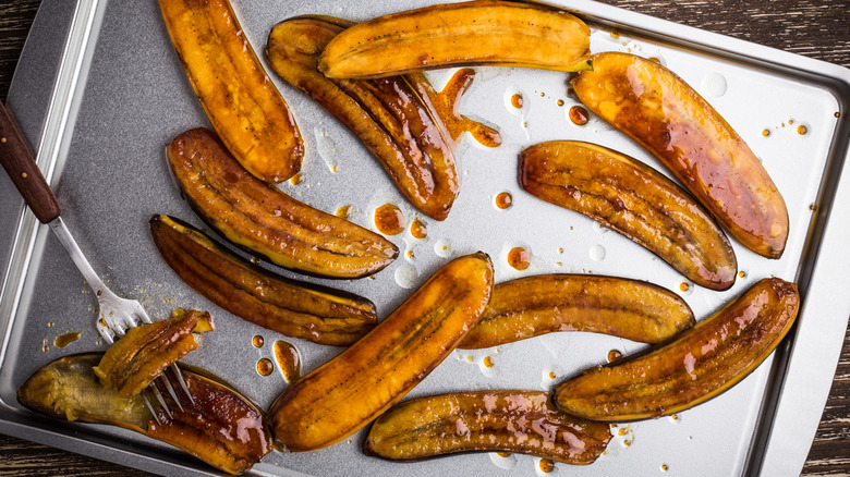 Roasted bananas are spread on a cooking pan.