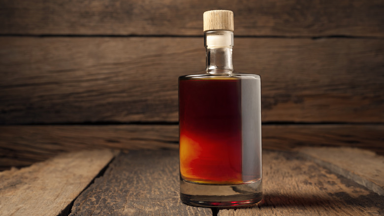 A bottle of bourbon sits on a wood table in front of wood paneling.