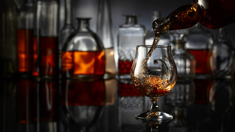 Brandy being poured into a glass with decanters in the background