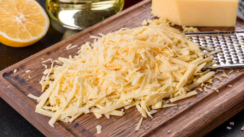 Grated white cheese on cutting board next to grater