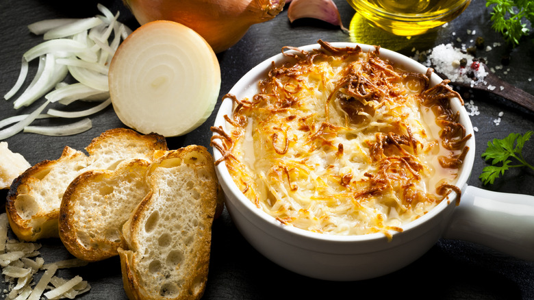 French onion soup in bowl next to toasted bread and sliced onion