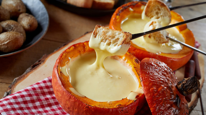 skewers dipping bread into melted cheese fondue in a roasted pumpkin