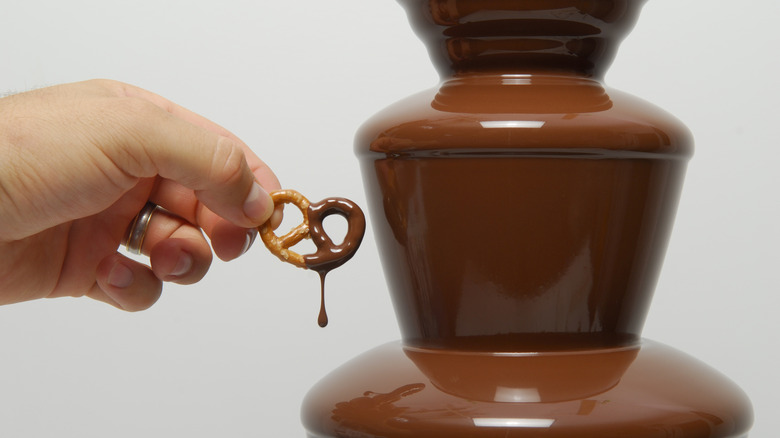 hand dipping a pretzel in a chocolate fountain