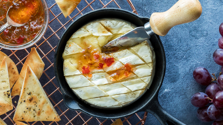 Melted brie in cast iron pan surrounded by pepper jelly and flatbreads