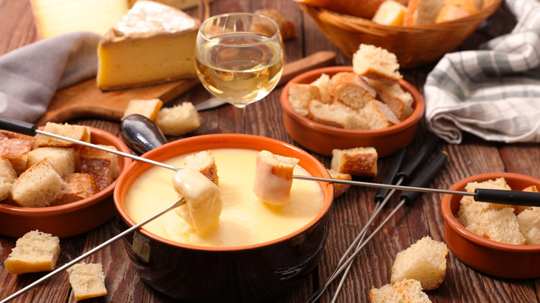 skewers dipping bread cubes into a bot of cheese fondue on dining table