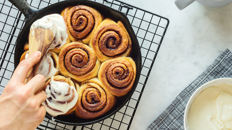 hand smearing frosting on cinnamon rolls