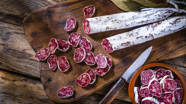 Sliced Spanish sausages on wooden cutting board with knife
