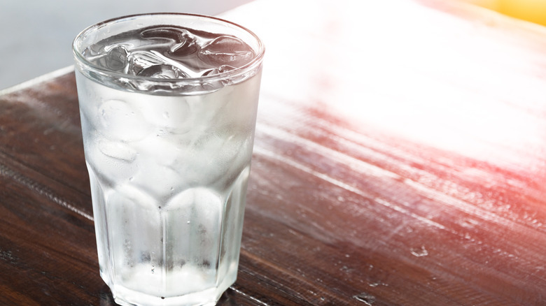 Chilled glass of water with ice cubes on wooden table