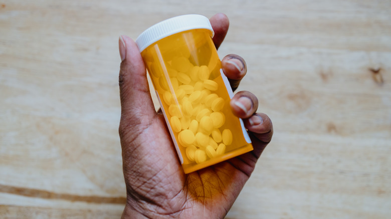 Hand holding medicine in orange prescription bottle